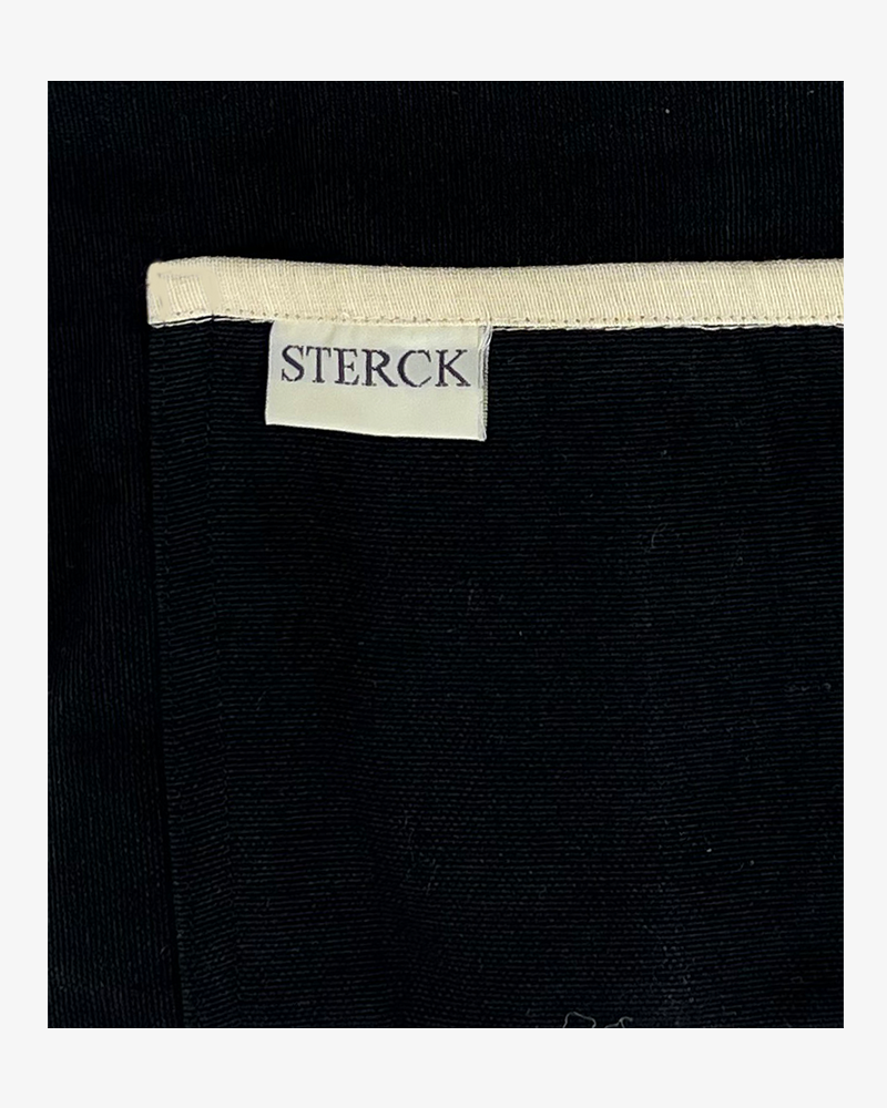 black apron with cream detailing and ties. double front pockets and adjustable neck strap. sterck and co. close up of pocket detailing and fabric.