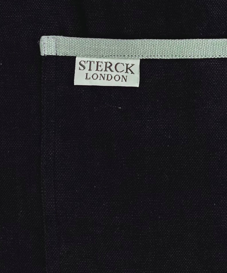 black apron with grey straps and grey trimmed double front pocket. adjustable neck strap. close up of colour and pocket detailing by sterck & co.