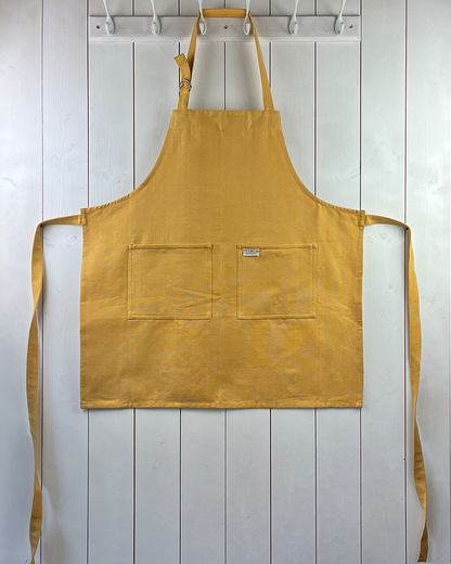 A sunflower yellow cotton apron with double front pockets and adjustable neck strap. Sterck & Co.