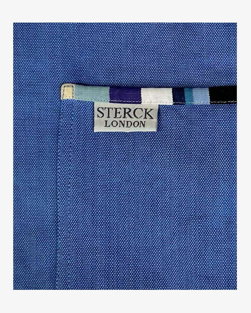 a bold blue cotton apron with stripy detailing. double front pockets, stripy ties and adjustable neck strap. sterck & co. caloosa sky. close up of fabric and pocket detailing.