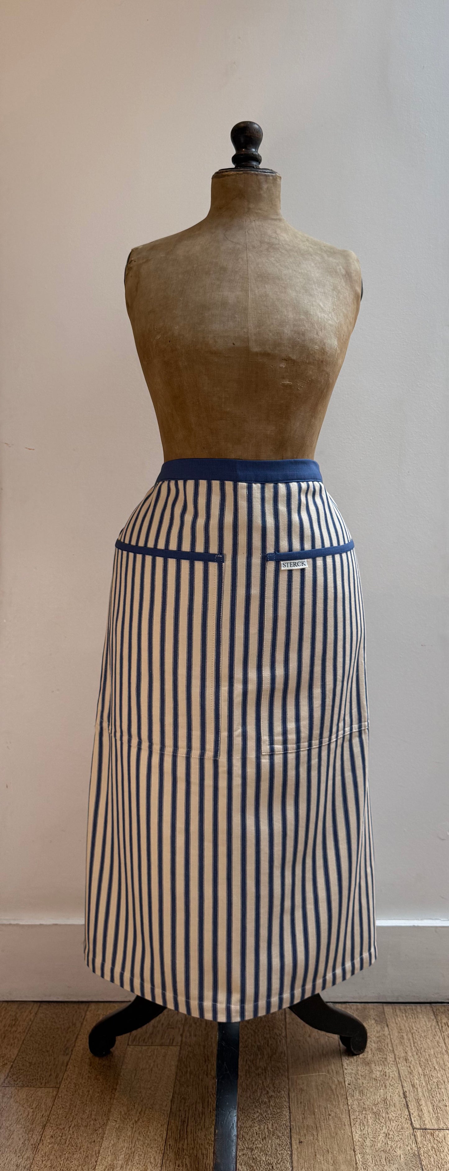sterck half apron in kolaba blue stripe, modelled by an antique mannequin. close up.