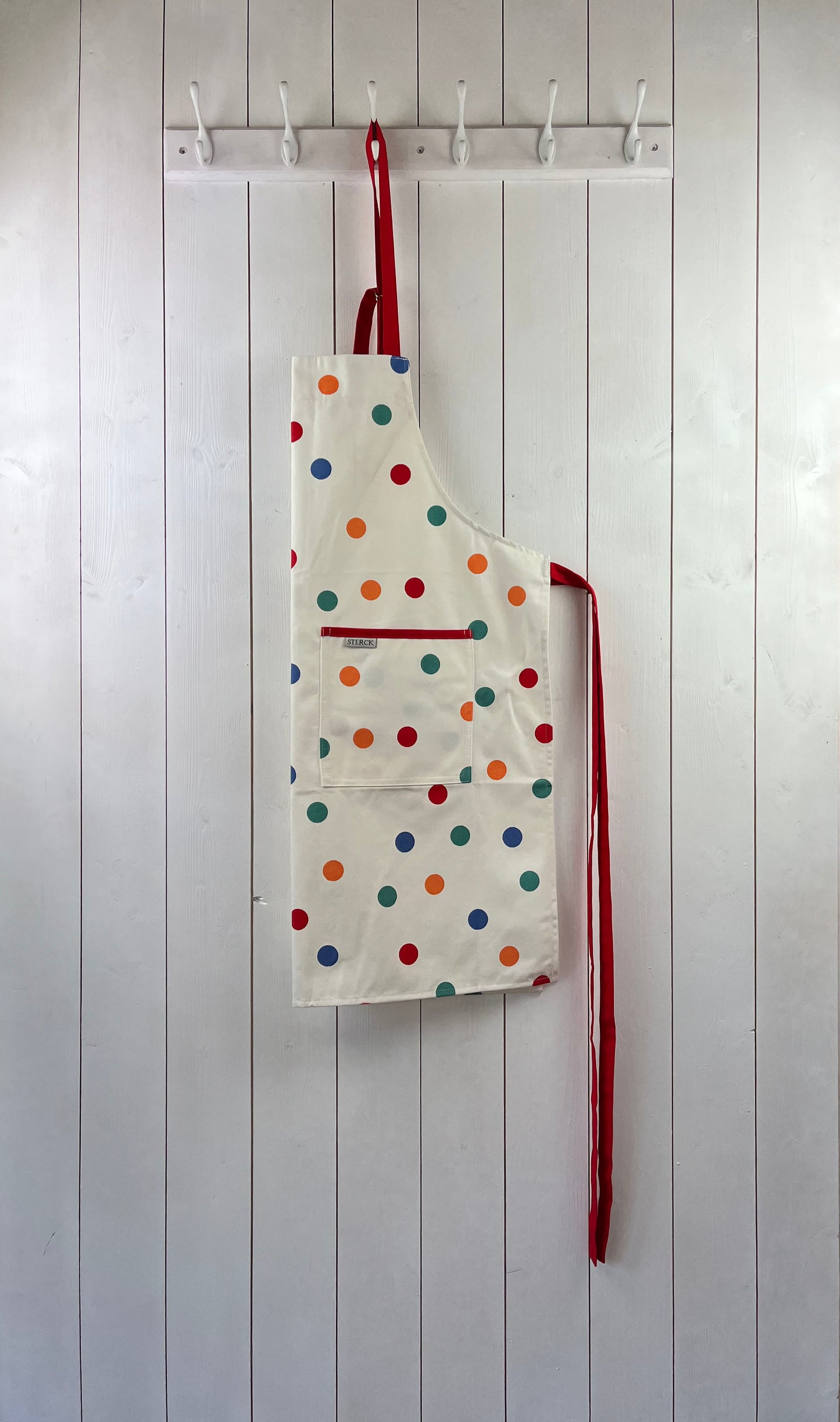 cream apron with multicoloured spots, double front pockets and red ties with adjustable neck strap.