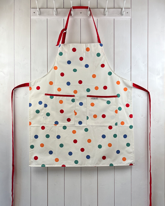 Cream apron with multicoloured spots, double front pockets and red ties with adjustable neck strap.