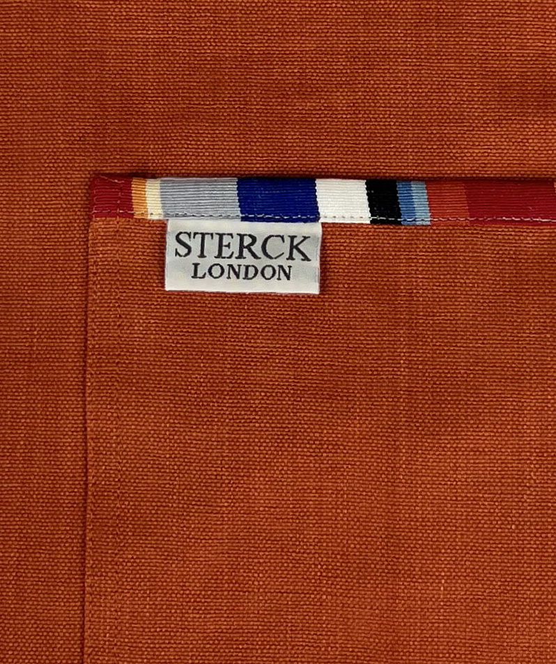 vibrant orange apron with stripey straps and edging. two front pockets and adjustable neck strap. close up of pocket detailing.