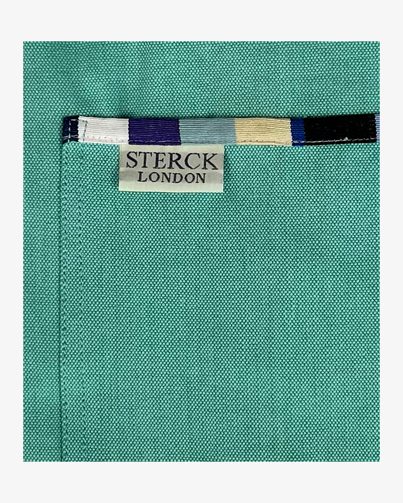 A mint green cotton apron with stripy detailing, double front pockets, stripy ties and adjustable neck strap. Sterck & Co. Close up of fabric and pocket detailing.