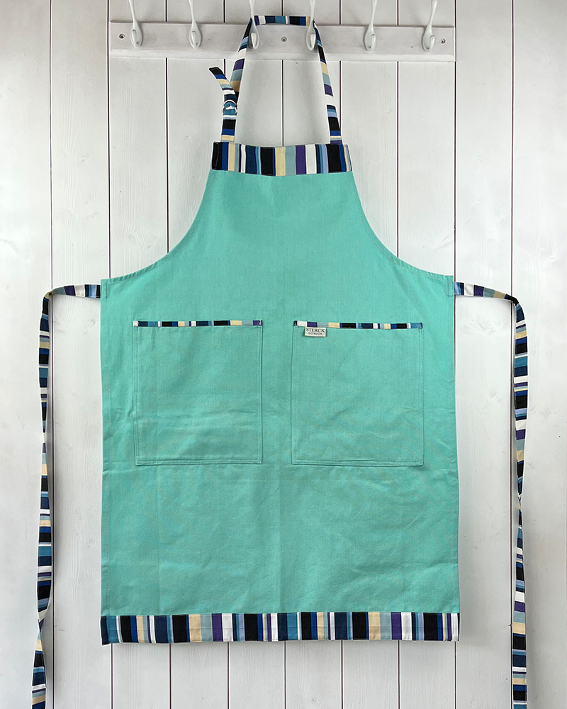 A mint green cotton apron with stripy detailing, double front pockets, stripy ties and adjustable neck strap. Sterck & Co.