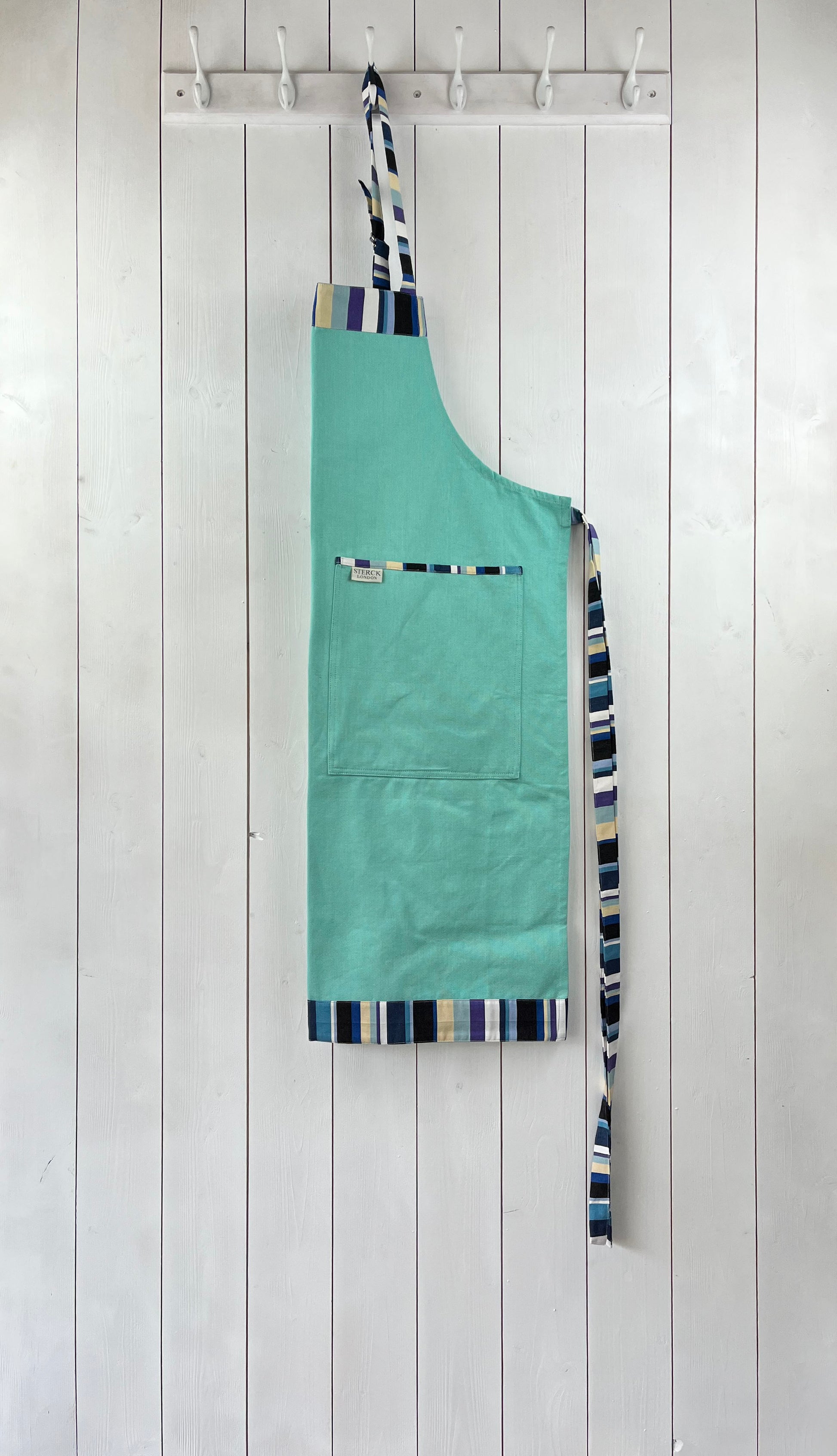 A mint green cotton apron with stripy detailing, double front pockets, stripy ties and adjustable neck strap. Sterck & Co.