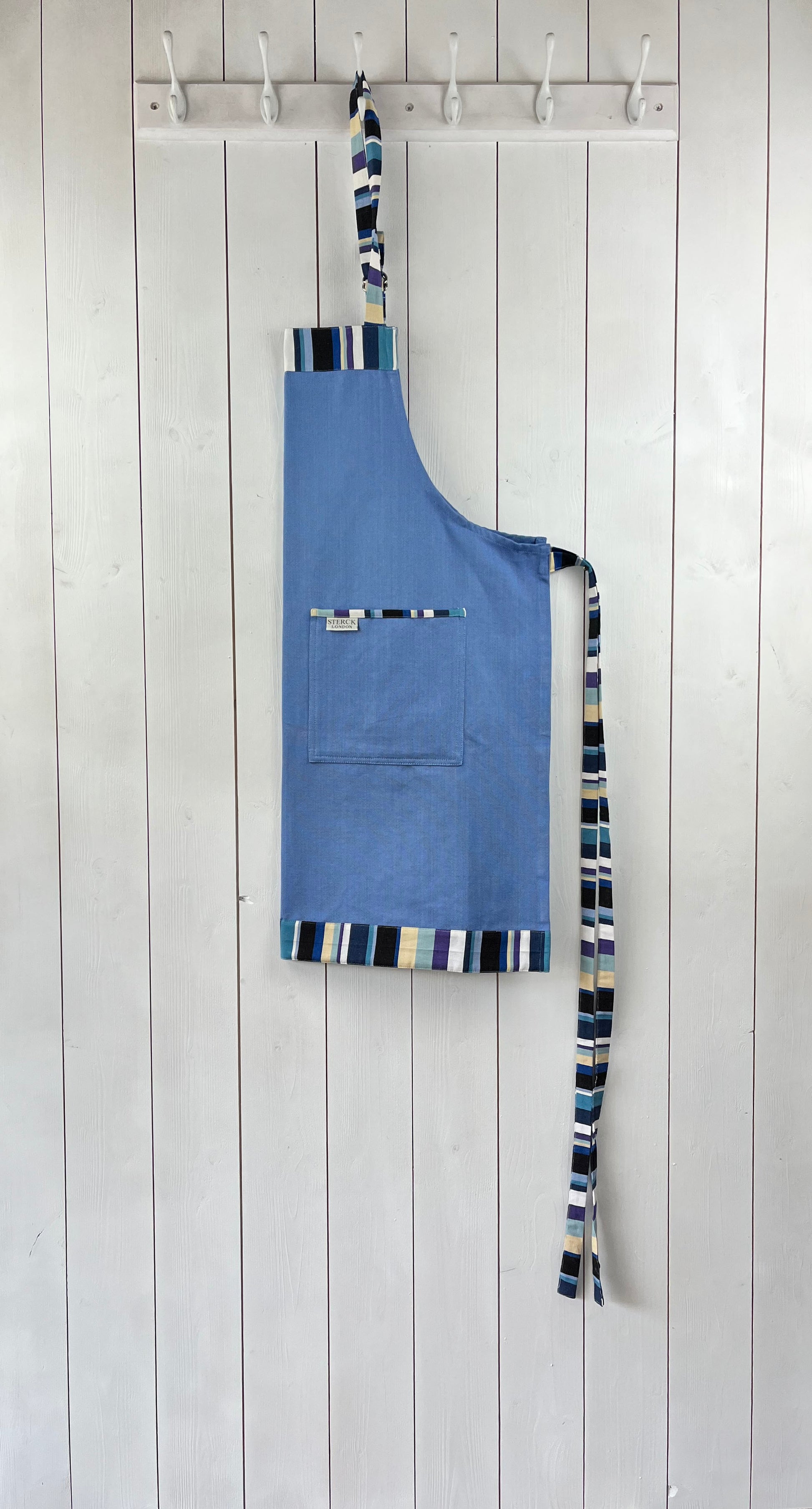 A bold blue cotton apron with stripy detailing. Double front pockets, stripy ties and adjustable neck strap. Sterck & Co. Caloosa Sky.