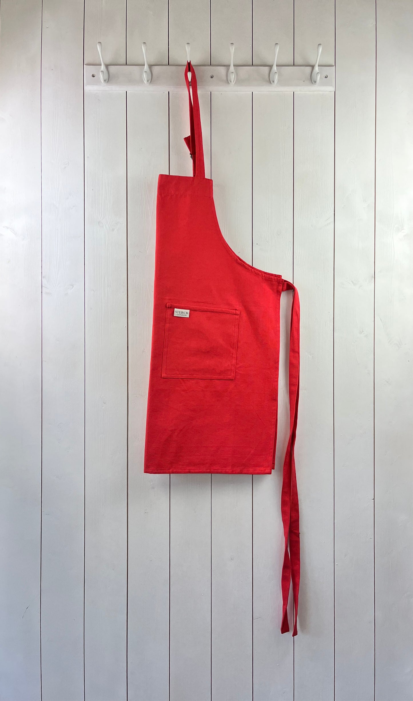 a poppy red cotton apron with double front pockets and adjustable neck strap. sterck & co.