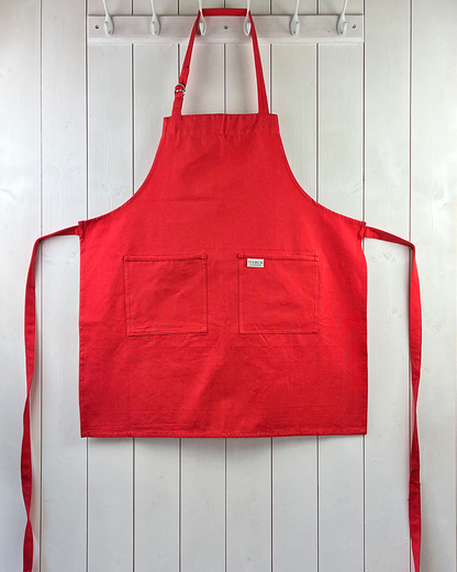 A poppy red cotton apron with double front pockets and adjustable neck strap. Sterck & Co.
