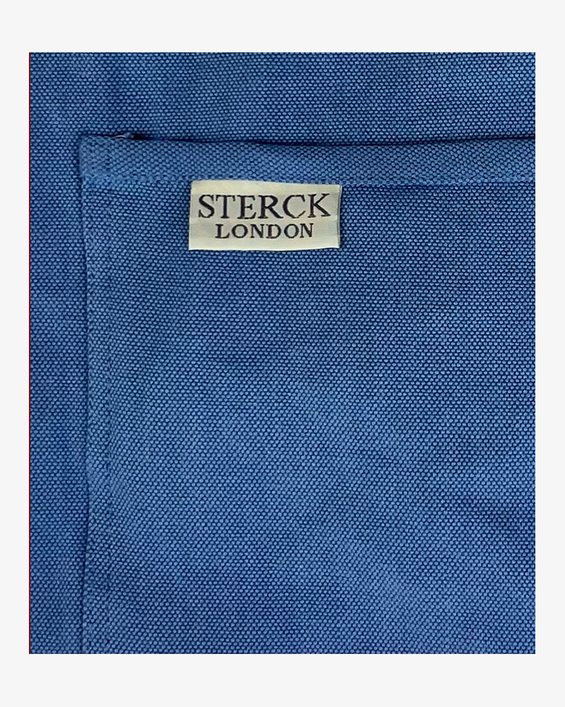 Sky blue cotton apron with double front pockets and adjustable neck strap. Sterck & Co. Close up of fabric and pocket detailing.