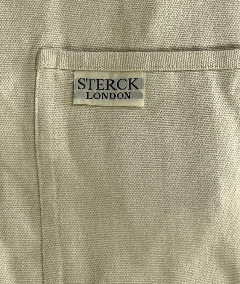 Alabaster white cotton apron with double front pockets and adjustable neck strap. Sterck & Co. Close up of fabric and pocket detailing.