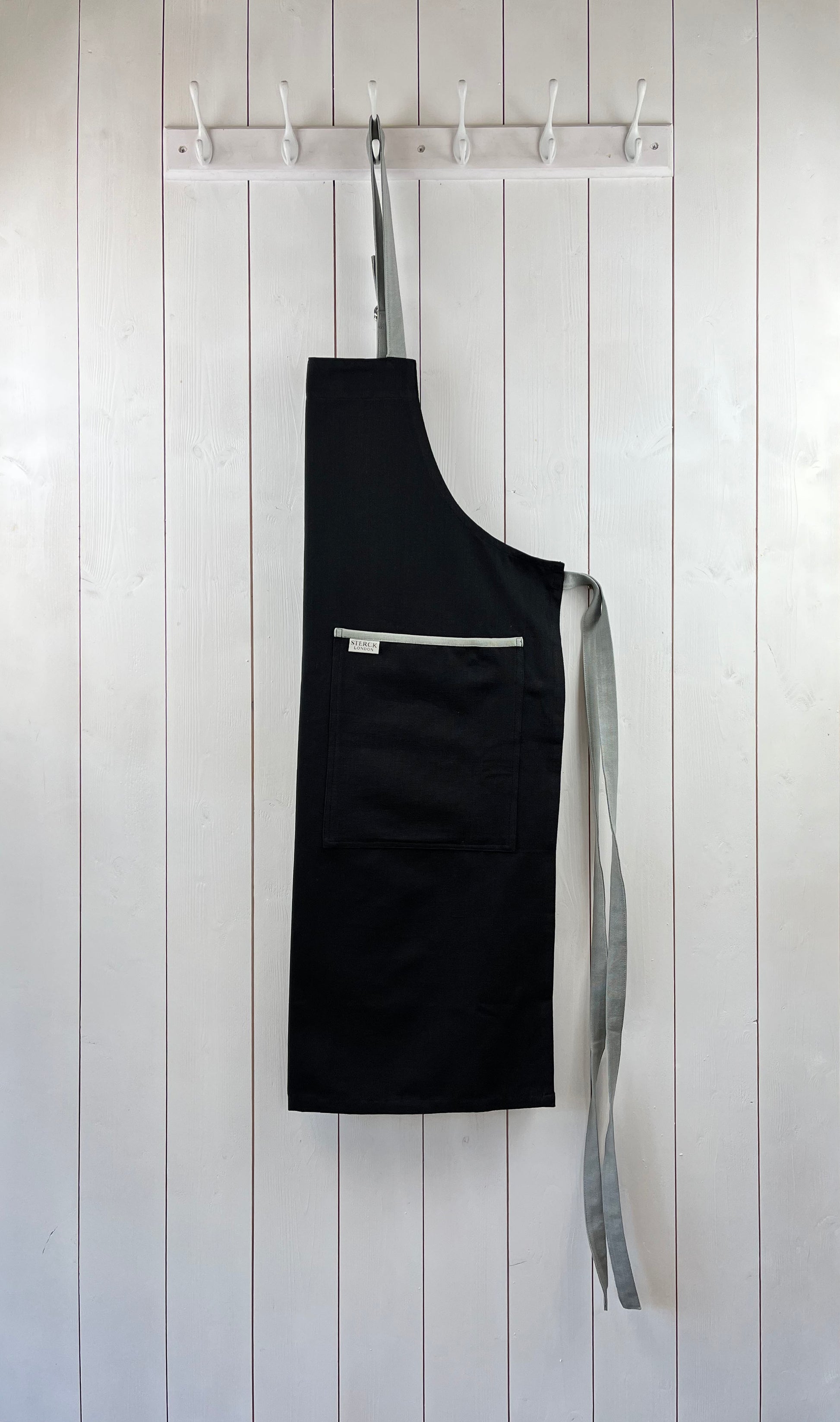 Black apron with grey straps and grey trimmed double front pocket. Adjustable neck strap.