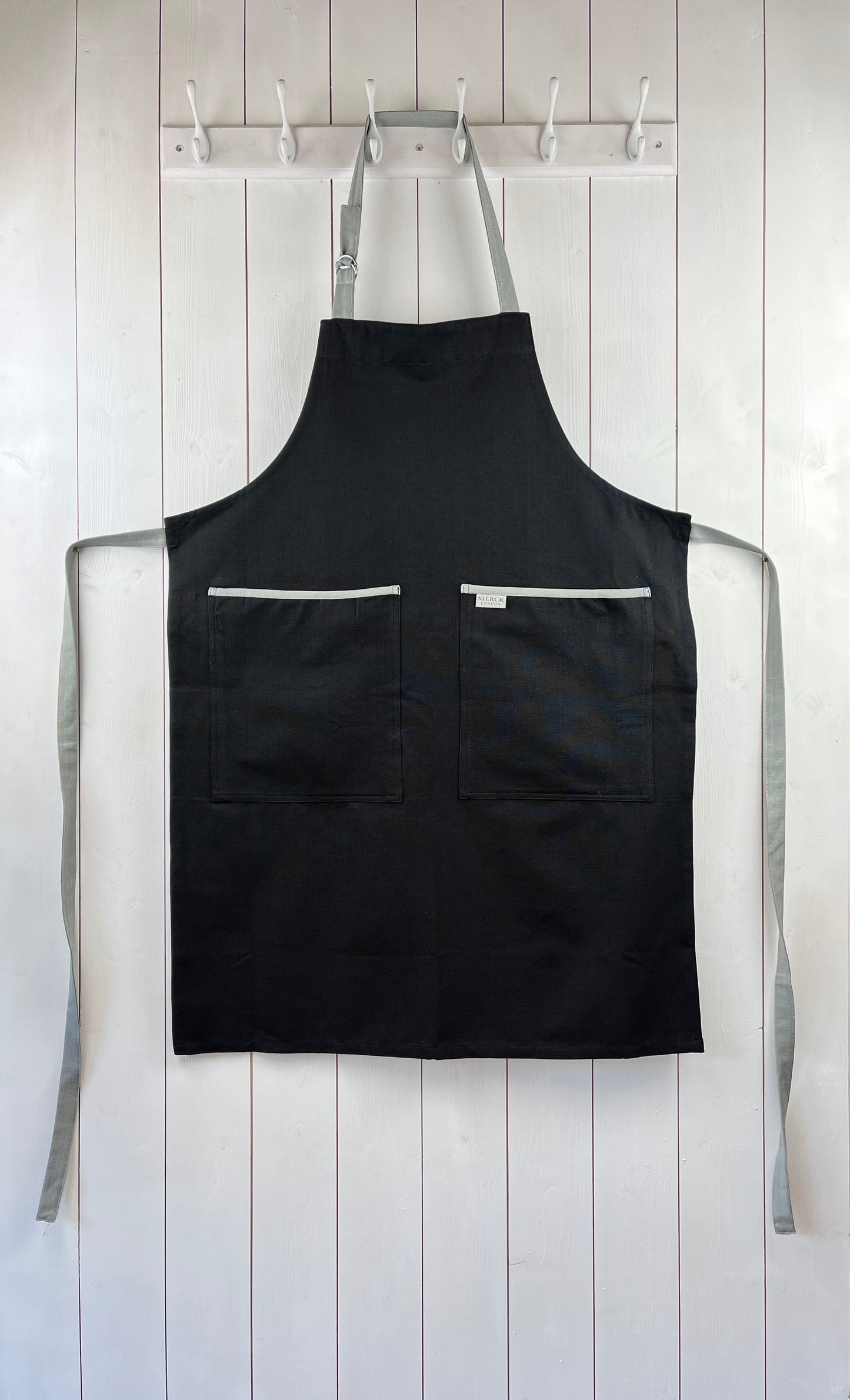 black apron with grey straps and grey trimmed double front pocket. adjustable neck strap.