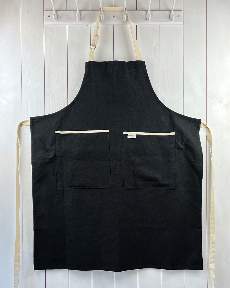 Black apron with cream detailing and ties. Double front pockets and adjustable neck strap. Sterck and Co.