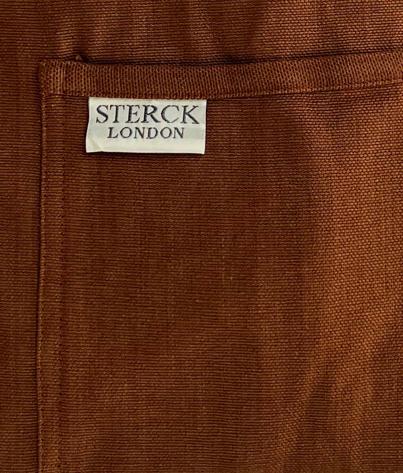 chocolate brown cotton apron with double front pockets and adjustable neck strap. sterck & co. close up of fabric and pocket detailing.