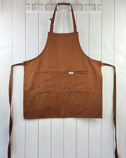 Chocolate brown cotton apron with double front pockets and adjustable neck strap. Sterck & Co.
