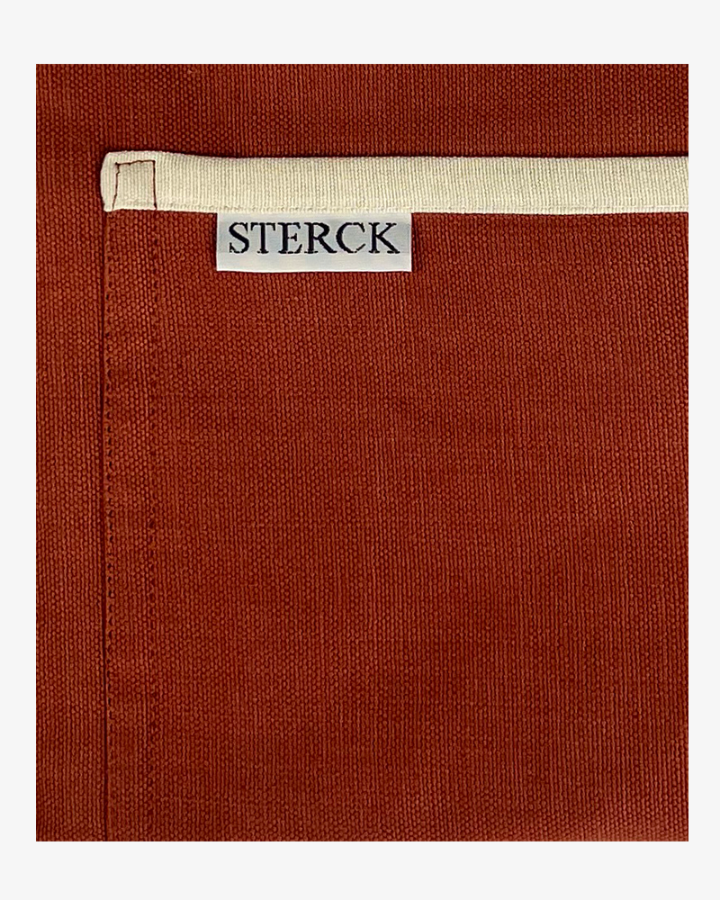 a dusky red apron with cream detailing, double front pockets and adjustable neck strap. sterck & co. close up of fabric and pocket detailing.