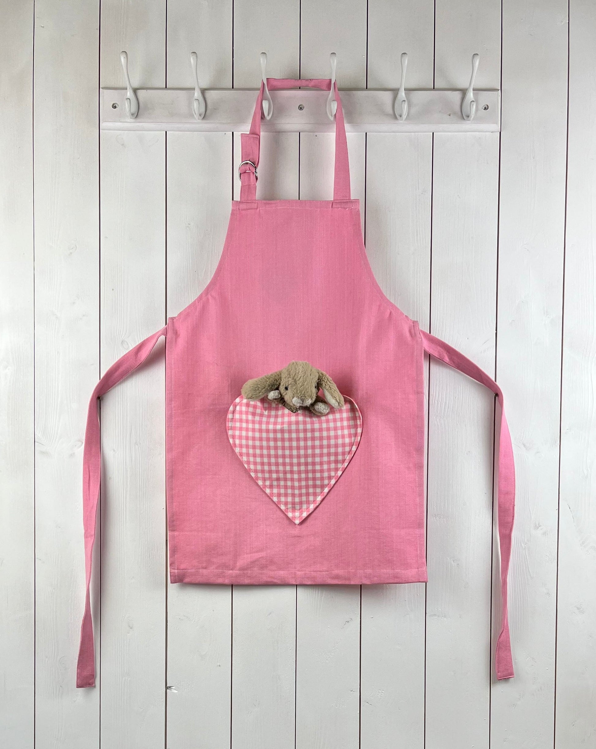 Pink child apron with gingham heart shaped pocket. From Sterck & Co. Rabbit not included.