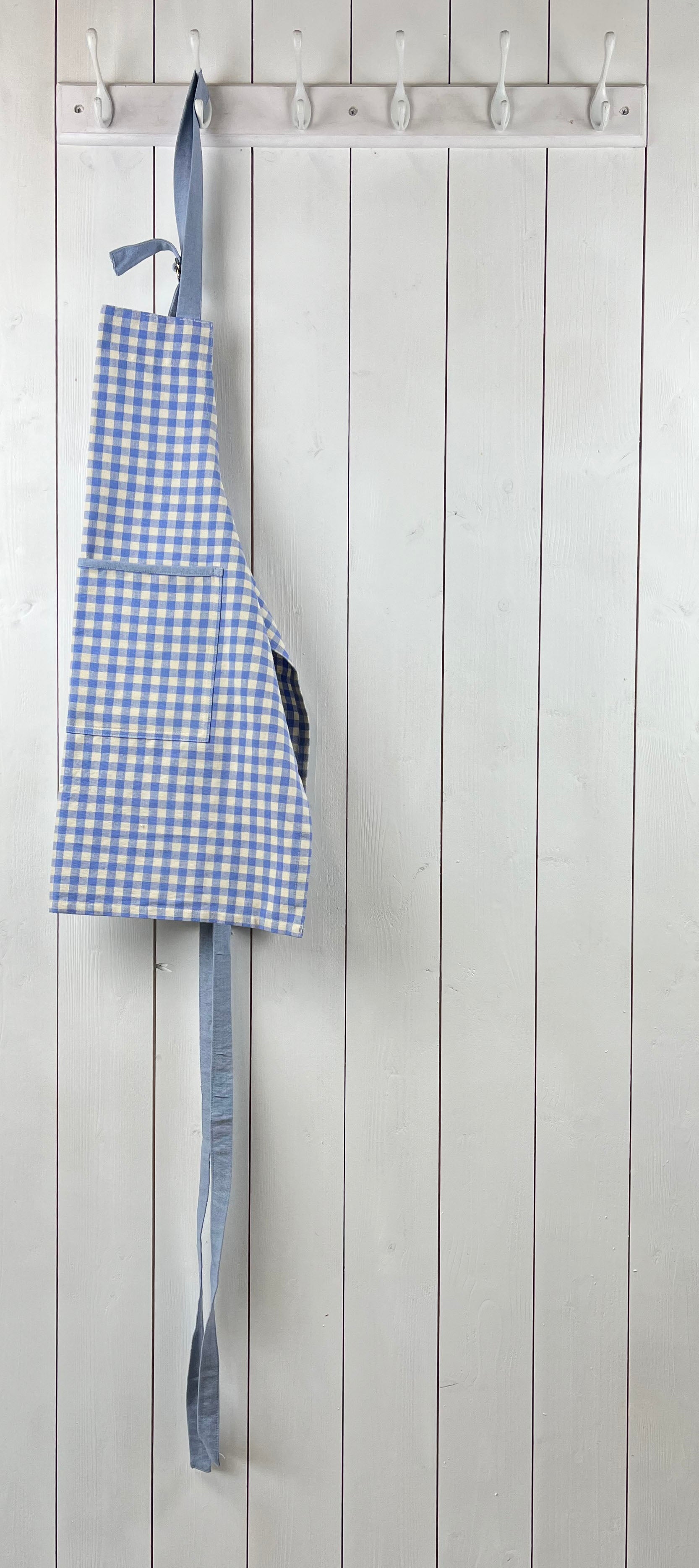 Blue gingham apron for children with large front pocket and adjustable neck strap. Sterck & Co.