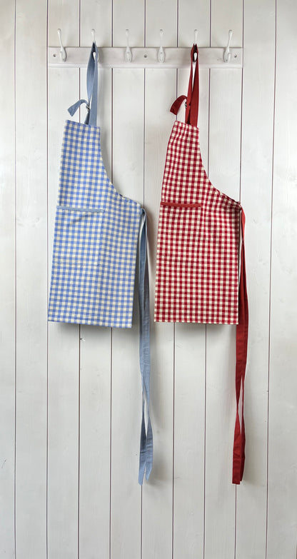 Child aprons in blue and red gingham with large front pockets and adjustable neck straps
