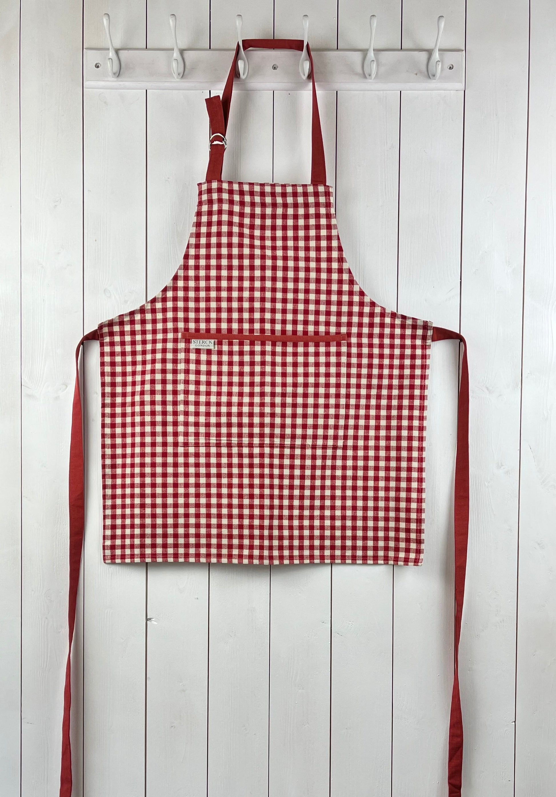 Red gingham apron for children with large front pocket and adjustable neck strap. Sterck & Co.