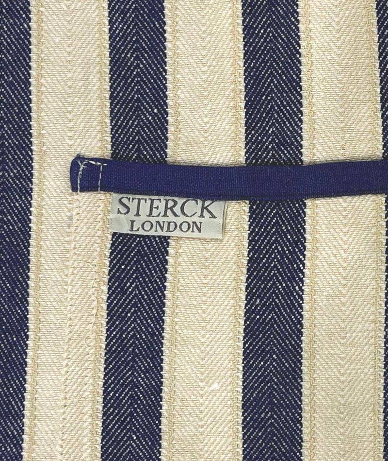 A classic wide striped cotton apron with double front pockets and adjustable neck tie. From Sterck & Co. Close up of fabric and pocket detailing.