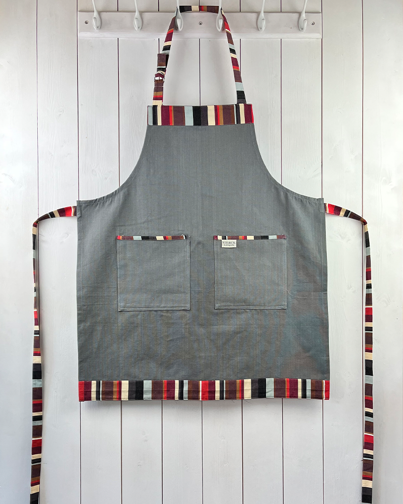 A bold grey cotton apron enlivened by stripey detailing. Double front pockets, stripy ties and adjustable neck strap. Sterck & Co.