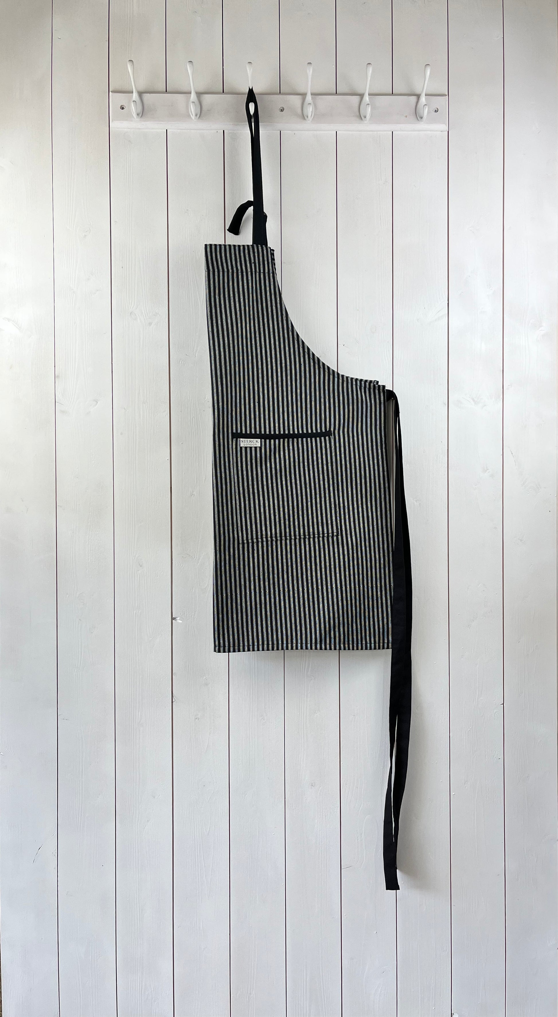 Black and white striped cotton apron with double front pockets, black ties and adjustable neck strap. Sterck & Co. Drum black.