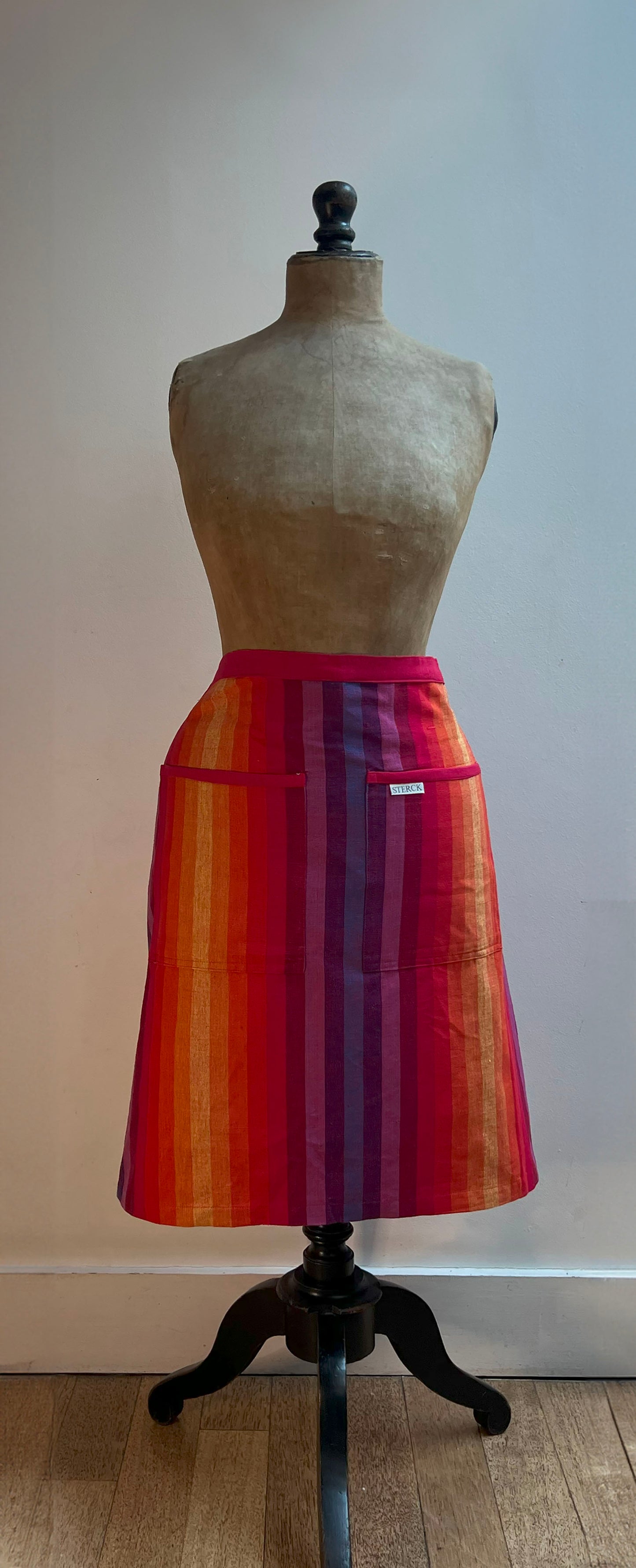 cotton rainbow striped half apron being worn by a mannequin. made from a durable pure cotton fabric in vibrant rainbow stripes branded by sterck & co