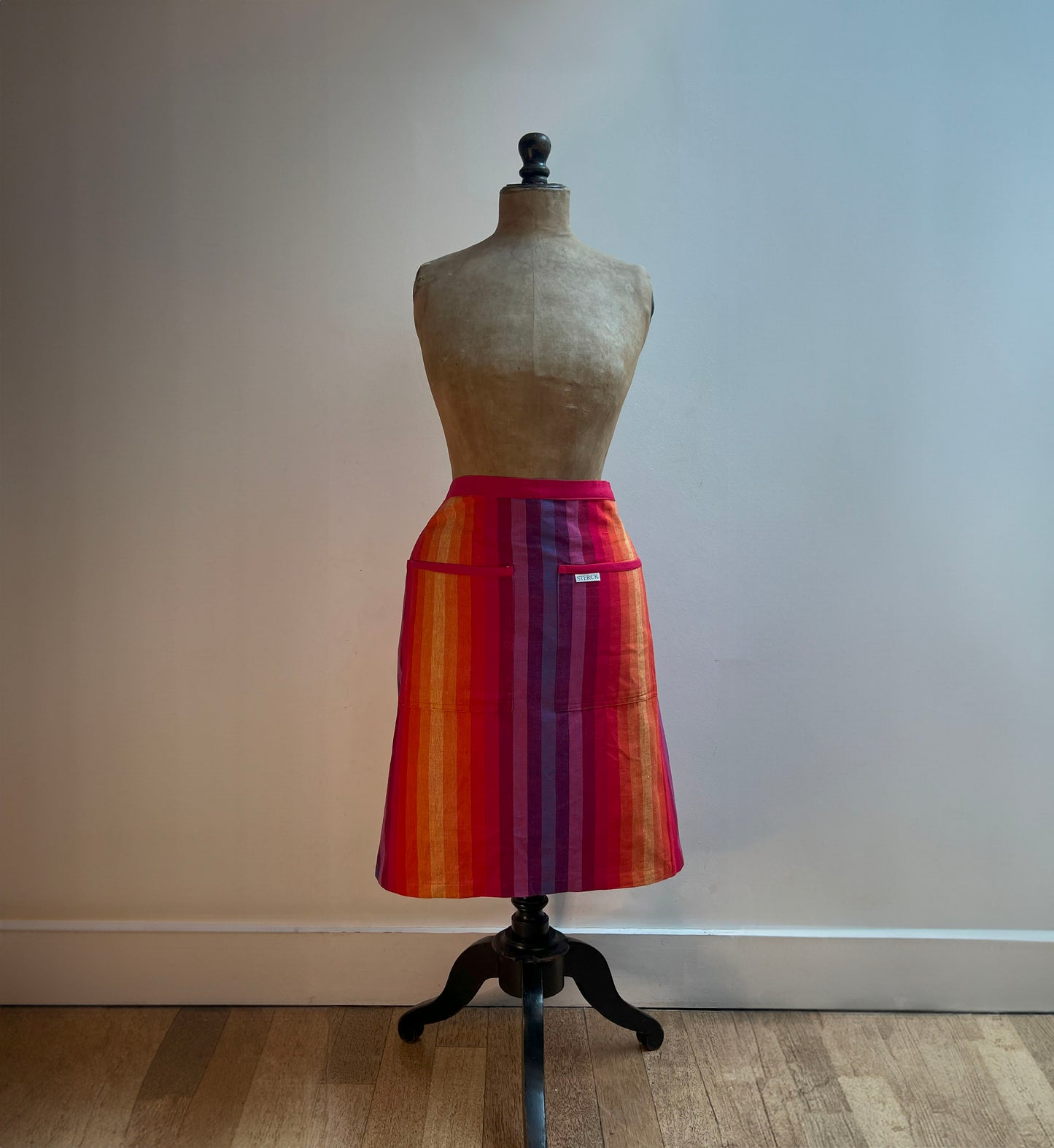 cotton rainbow striped half apron being worn by a mannequin.  made from a durable  pure cotton fabric in vibrant rainbow stripes branded sterck & co