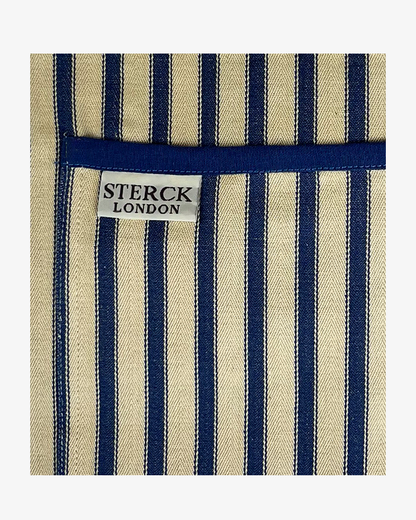 A classic cream and blue striped cotton apron with double front pockets, blue ties and adjustable neck straps. Sterck & Co. Close up of fabric and pocket detailing.