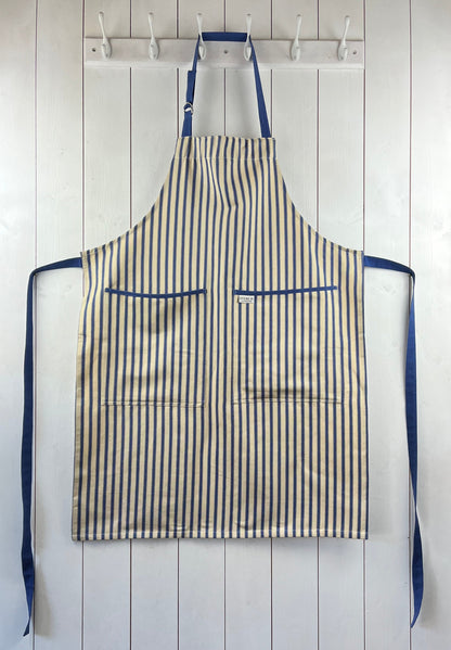A classic cream and blue striped cotton apron with double front pockets, blue ties and adjustable neck straps. Sterck & Co.