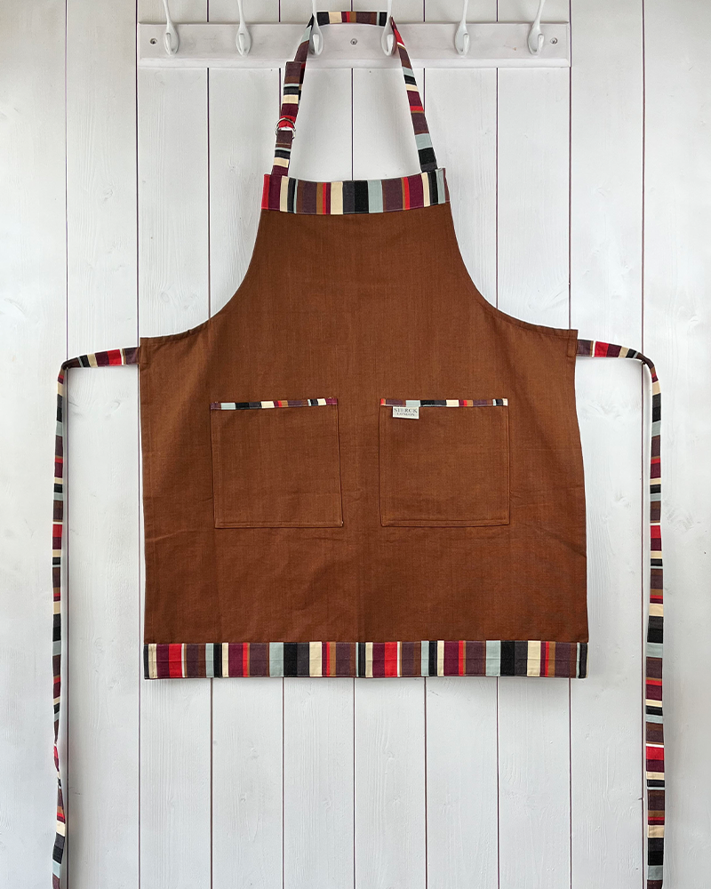 a brown cotton apron with stripy detailing, double front pockets, striped ties and adjustable neck strap. sterck & co.