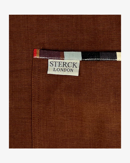 A brown cotton apron with stripy detailing, double front pockets, striped ties and adjustable neck strap. Sterck & Co. Close up of fabric and pocket detailing.