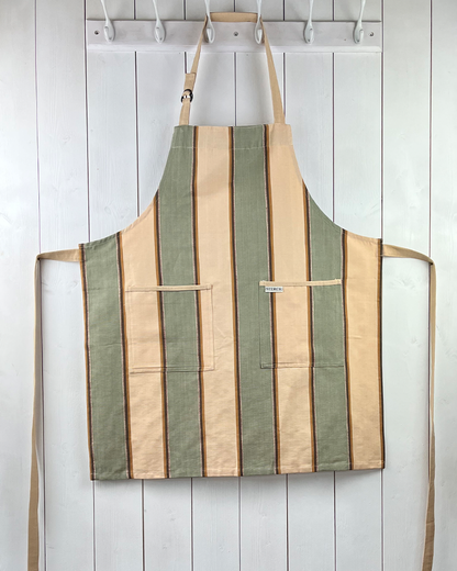 Wide striped, cream, green and brown cotton apron with double pockets, cream ties and adjustable neck strap. Sterck & Co.