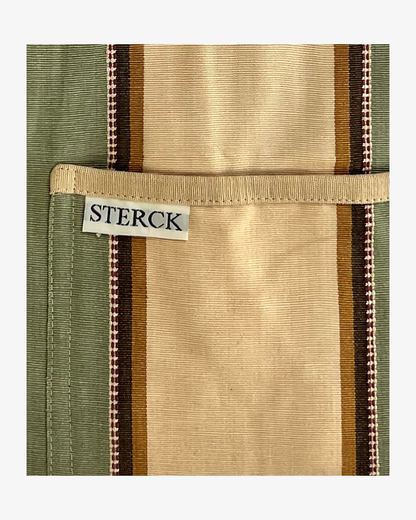 Wide striped, cream, green and brown cotton apron with double pockets, cream ties and adjustable neck strap. Sterck & Co. Close up of fabric and pocket detailing.