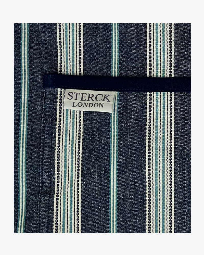 A classic blue striped cotton apron with double front pockets, blue ties and adjustable neck strap. Sterck & Co. Close up of fabric and pocket detailing.