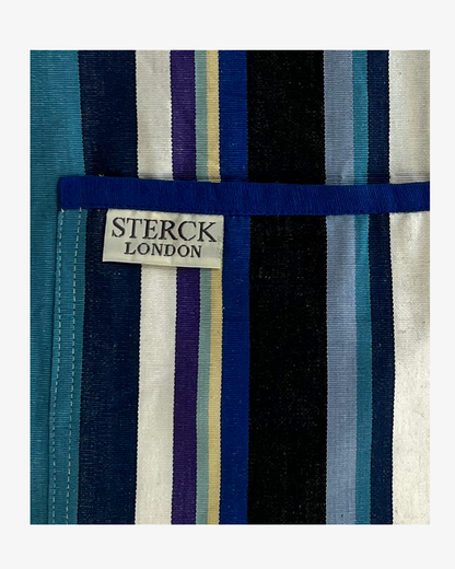 A modern and stylish blue stripy apron with double front pockets, blue ties and adjustable neck strap. 100% cotton. Sterck & Co. Close up of fabric and pocket details.