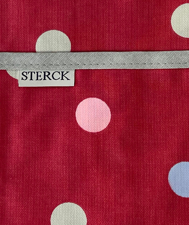 Pink cotton apron with coloured polka dots, grey ties and adjustable neck strap. Close up of fabric and pocket detail.