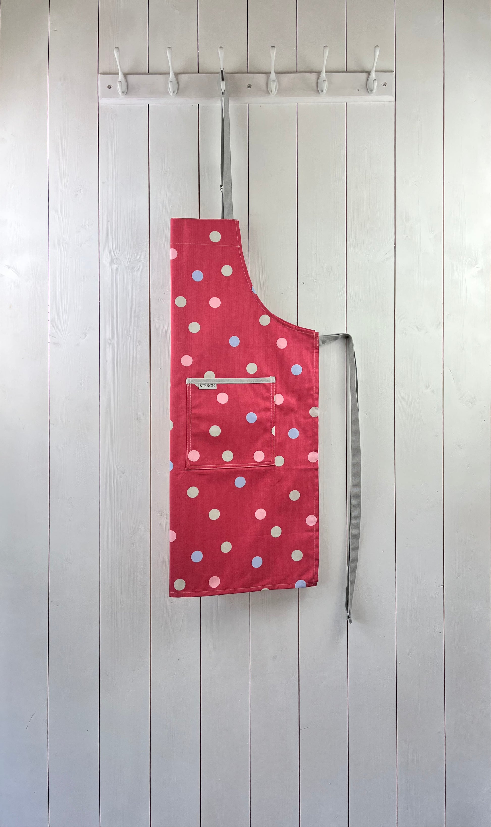 Pink cotton apron with coloured polka dots, grey ties and adjustable neck strap.