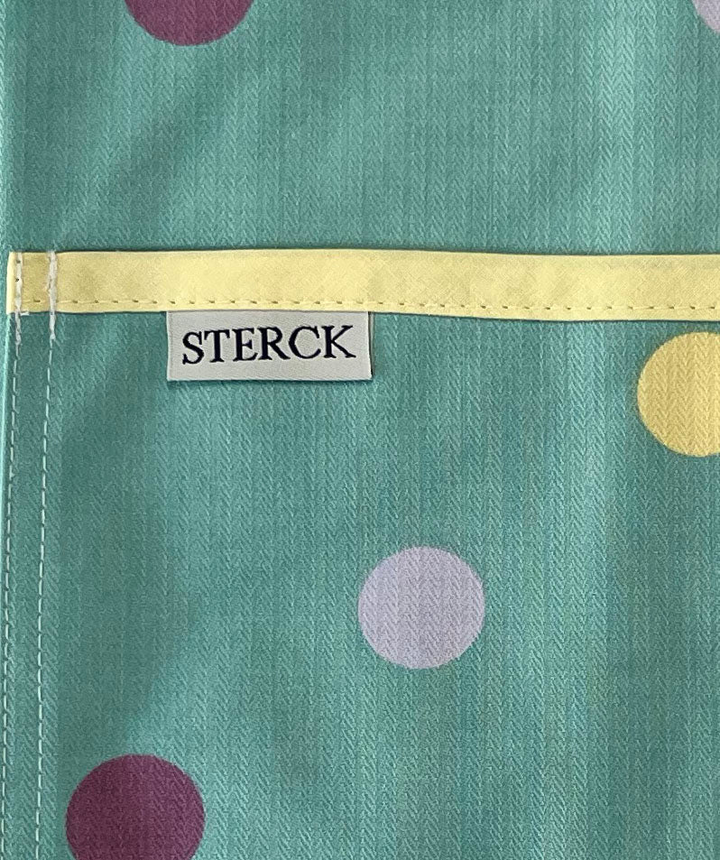 duck egg blue cotton apron with purple, yellow and mauve spots, yellow ties and adjustable neck strap. close up of fabric and pocket detail.