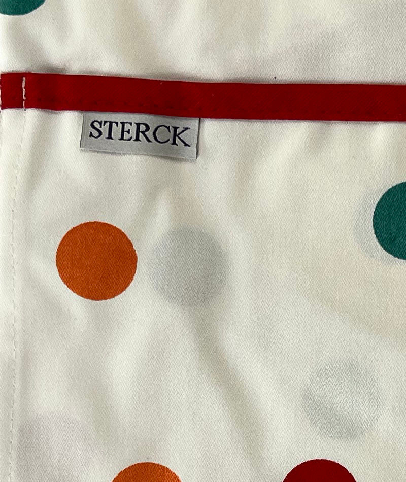 cream apron with multicoloured spots. close up of fabric and pocket detailing. 