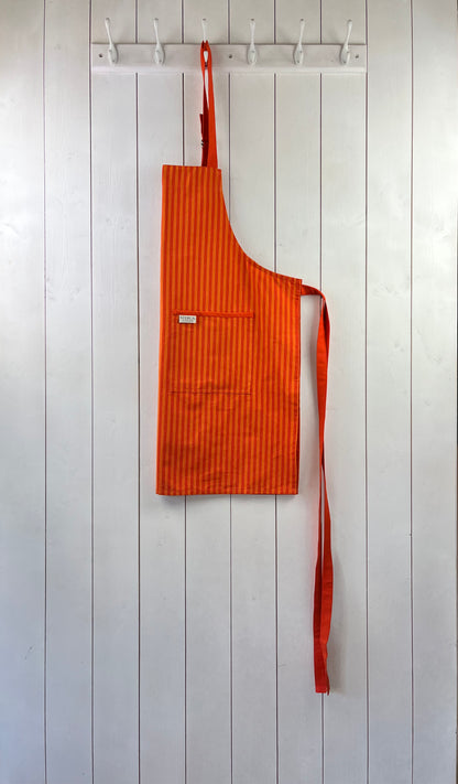 A bold striped orange cotton apron with double front pockets, orange staps and adjustable neck tie. Sterck & Co.