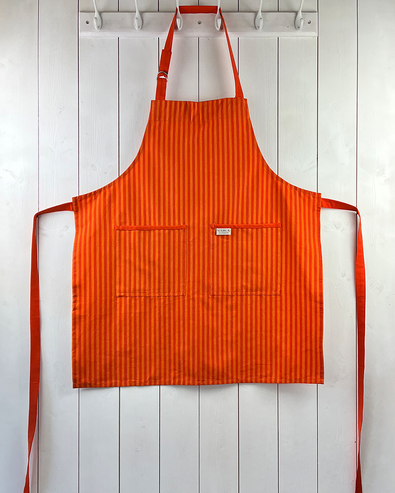 A bold striped orange cotton apron with double front pockets, orange staps and adjustable neck tie. Sterck & Co.
