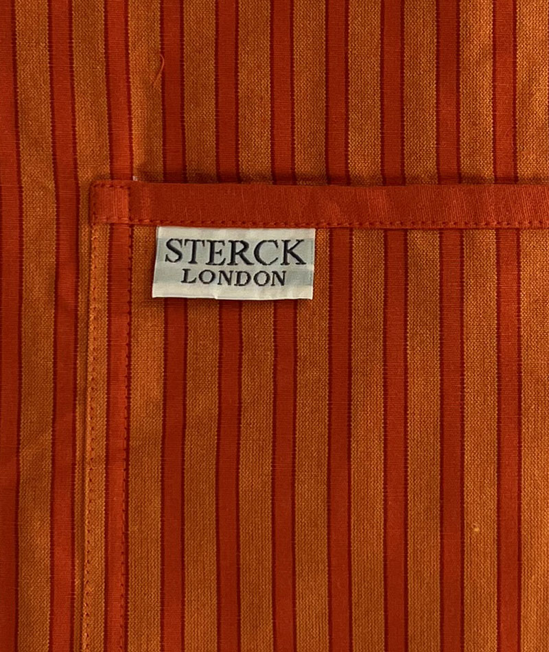 a bold striped orange cotton apron with double front pockets, orange staps and adjustable neck tie. sterck & co. close up of fabric and pocket detailing.
