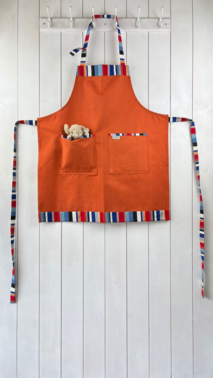 Vibrant orange apron with stripey straps and edging. Two front pockets and adjustable neck strap. Cuddly toy not included!